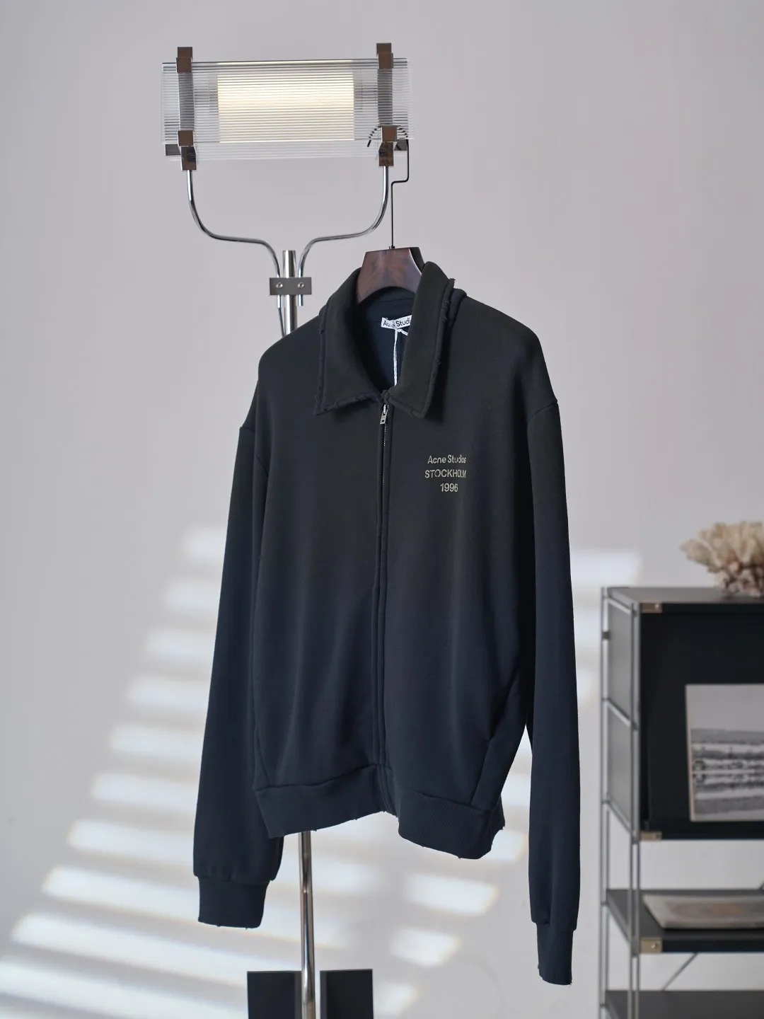 [Real auction] Acne Studios Retro distressed letter print zipper jacket [In Stock] Logo stamp at front, side-seam pockets, and ribbed cuffs and hem. Regular fit, just above the waist. It adopts a 3-strand composite fleece structure with 32 counts for the top layer and 40 counts for the bottom layer, with a weight of g/㎡. The 32-count yarn on the top layer is fine and smooth, giving the surface a smooth touch and excellent anti-pilling properties; the 40-count 3-ply yarn on the bottom layer is treated with a raising process to form a rich and soft fluff layer, providing excellent warmth and skin-friendly wrapping. With 21 2×2 ribs, the g/㎡ weight ensures that the collar, cuffs and hem have excellent tensile fatigue resistance and shape retention capabilities. During piece dyeing, the entire fabric is immersed in the dye vat after weaving, and the dye molecules fully penetrate into the fibers, ensuring full, deep colors and excellent color fastness. Each batch of dyeing produces subtle differences, making the color tone of the single product unique. On this basis, the paint is sprayed irregularly on the surface of the garment through manual spray painting to create a splash-like retro effect. The distressed processing of holes causes the color to fade and mottle in parts. The ribbed trim is also treated to form slight whitening and fluffing, which visually echoes the spray-painted effect on the body, making the new clothes appear as if they have been worn for a long time and exposed to the sun. The front logo stamp uses a slurry printing process. The printing slurry contains a special microcapsule foaming agent. After being baked at high temperature, the slurry layer expands to form three-dimensional bulges, and the surface presents a granular texture similar to inkjet paint. This process simulates the effect of random drops of pigment after being atomized during spray gun spraying. The edges of the pattern present a natural feathering transition, rather than the rigid boundaries of glue printing. The printing surface has a fine graininess and soft elasticity to the touch, forming a closed loop of the process with the distressed effect of the spray painting on the body.